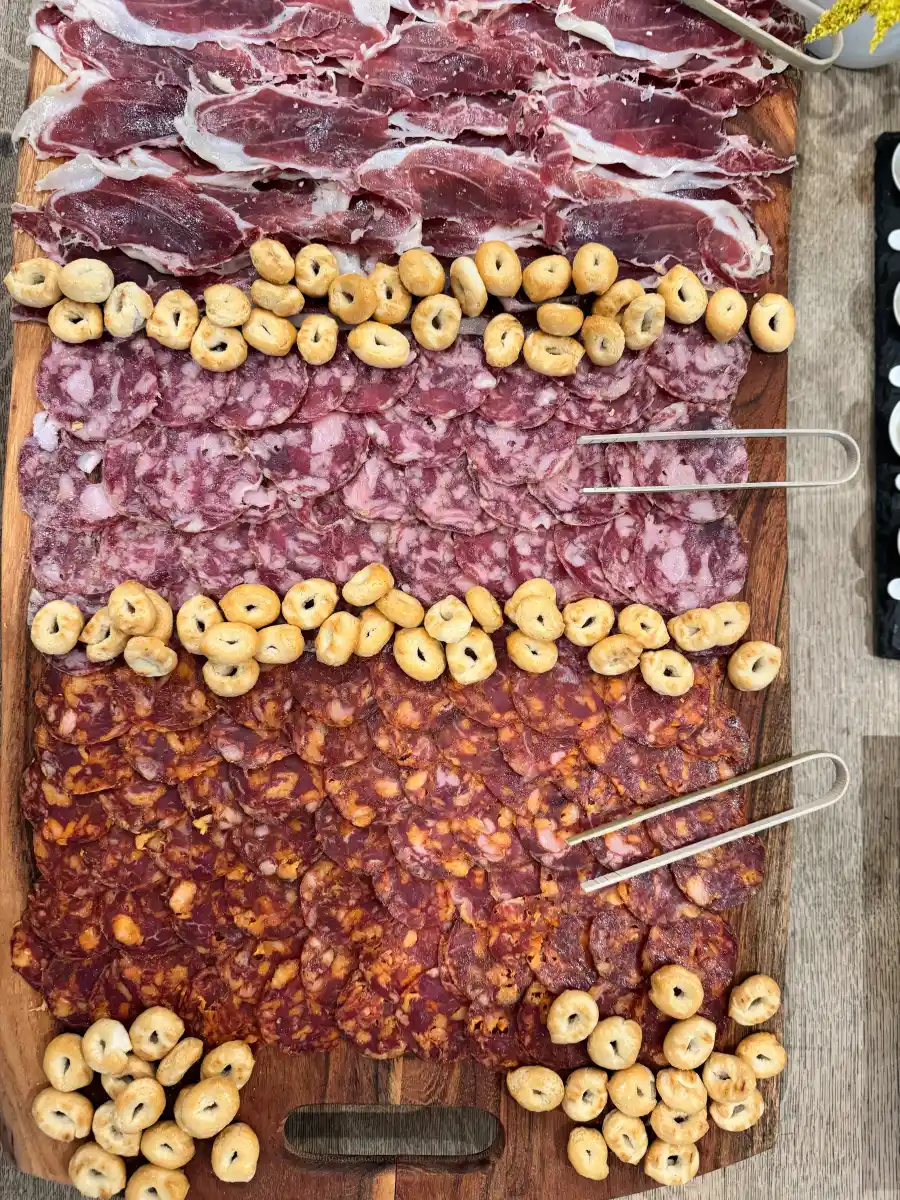 Three-cut Spanish charcuterie spread — jamón ibérico, salchichón ibérico, chorizo ibérico — laid out on a wooden board with picos crackers at a Cantábrico event in Houston