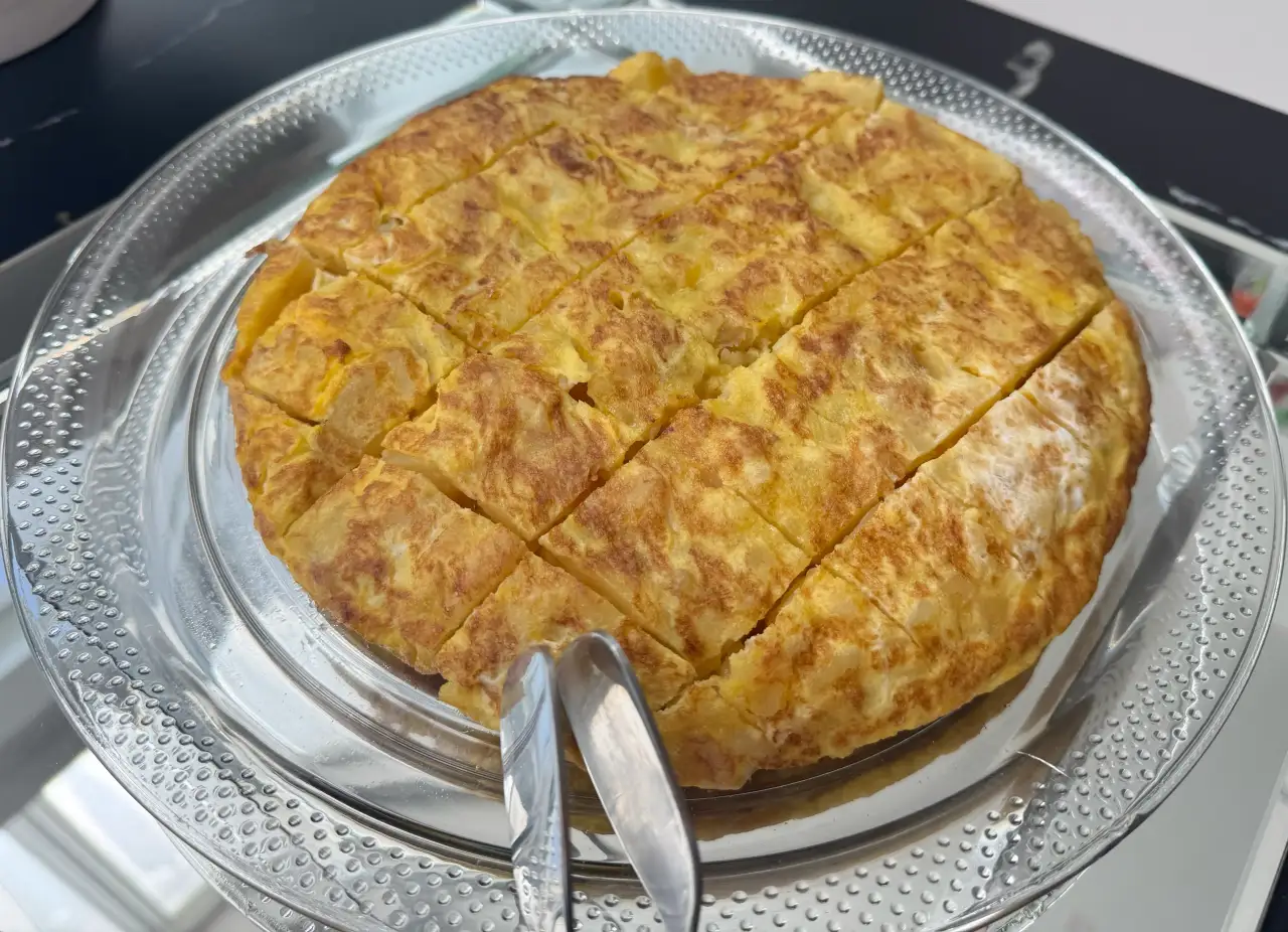 Whole Spanish tortilla de patatas sliced into squares on a glass plate, ready to serve — Cantábrico, Houston