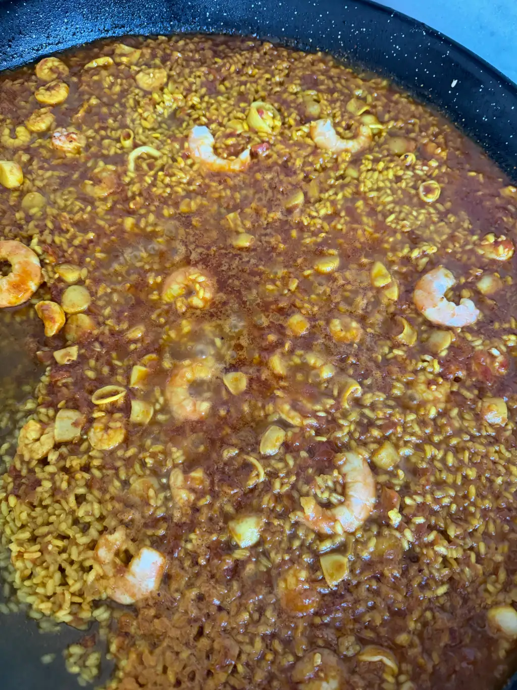 Paella mid-cooking with broth still visible around the rice and shrimp, the moment before the socarrat forms